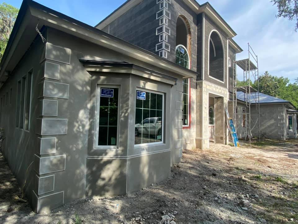 Exterior of a house under construction with stucco walls, arched windows, and a small side extension.