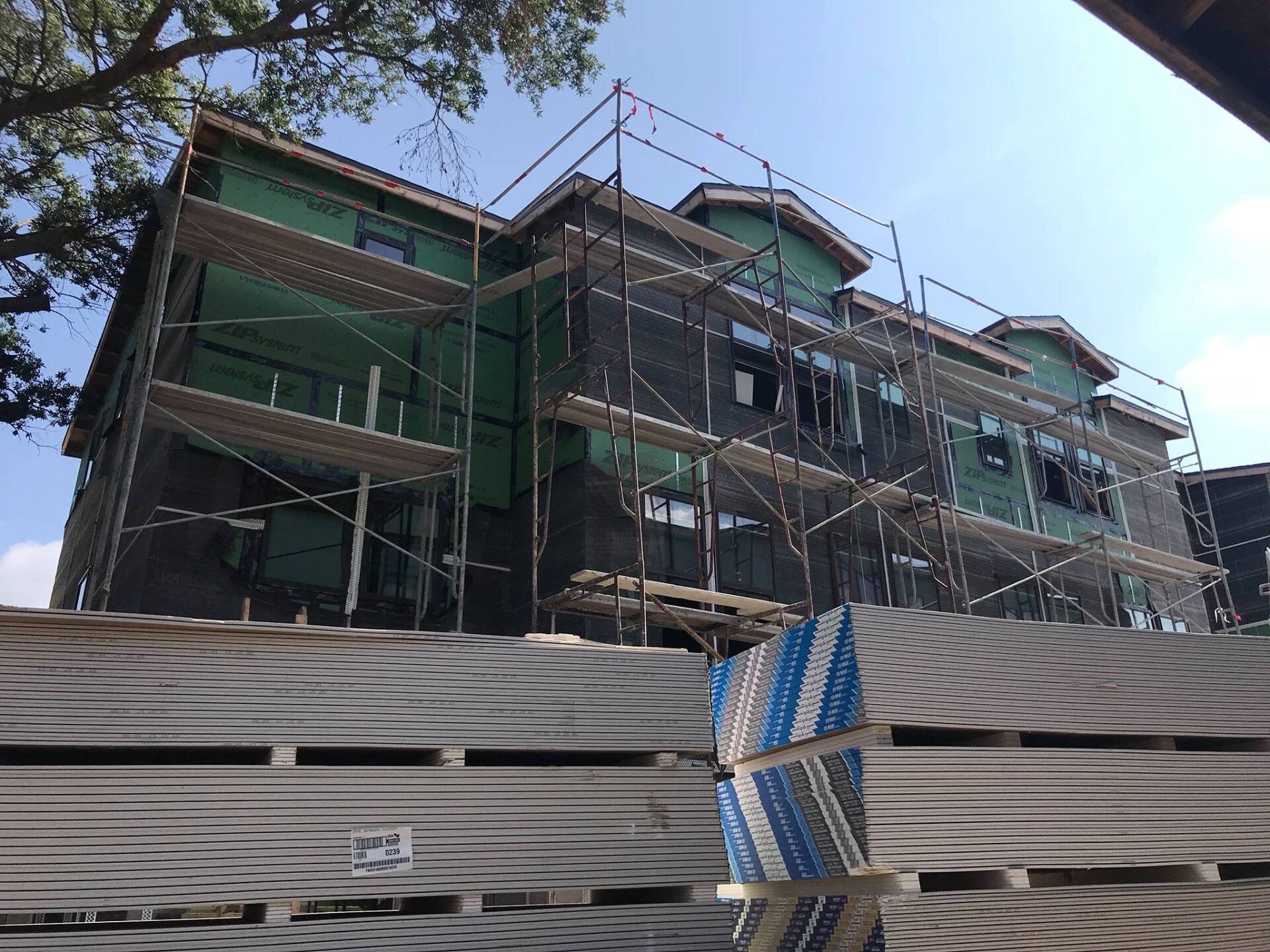 Building under construction with scaffolding and green and black wrap. Gray pallets in foreground.