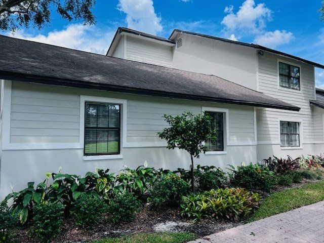 Light gray building with white trim, black roof, green plants, and blue sky.