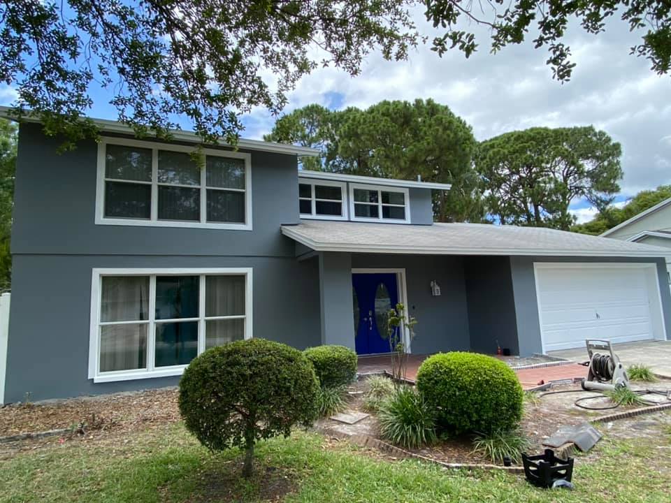 Two-story gray house with white trim, blue door, and white garage door, under a cloudy sky.