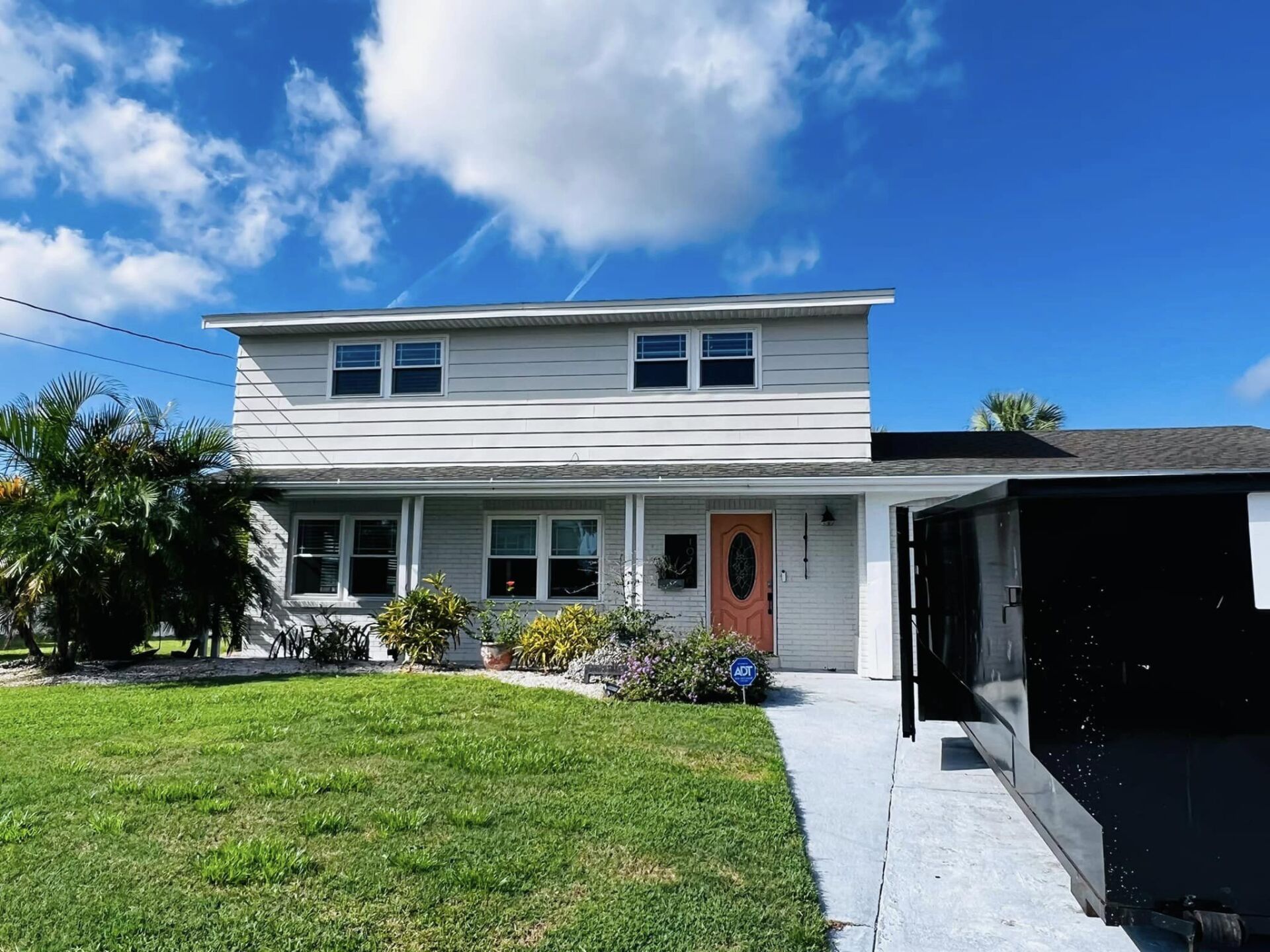 Two-story white house with pink front door, green lawn, and blue sky.