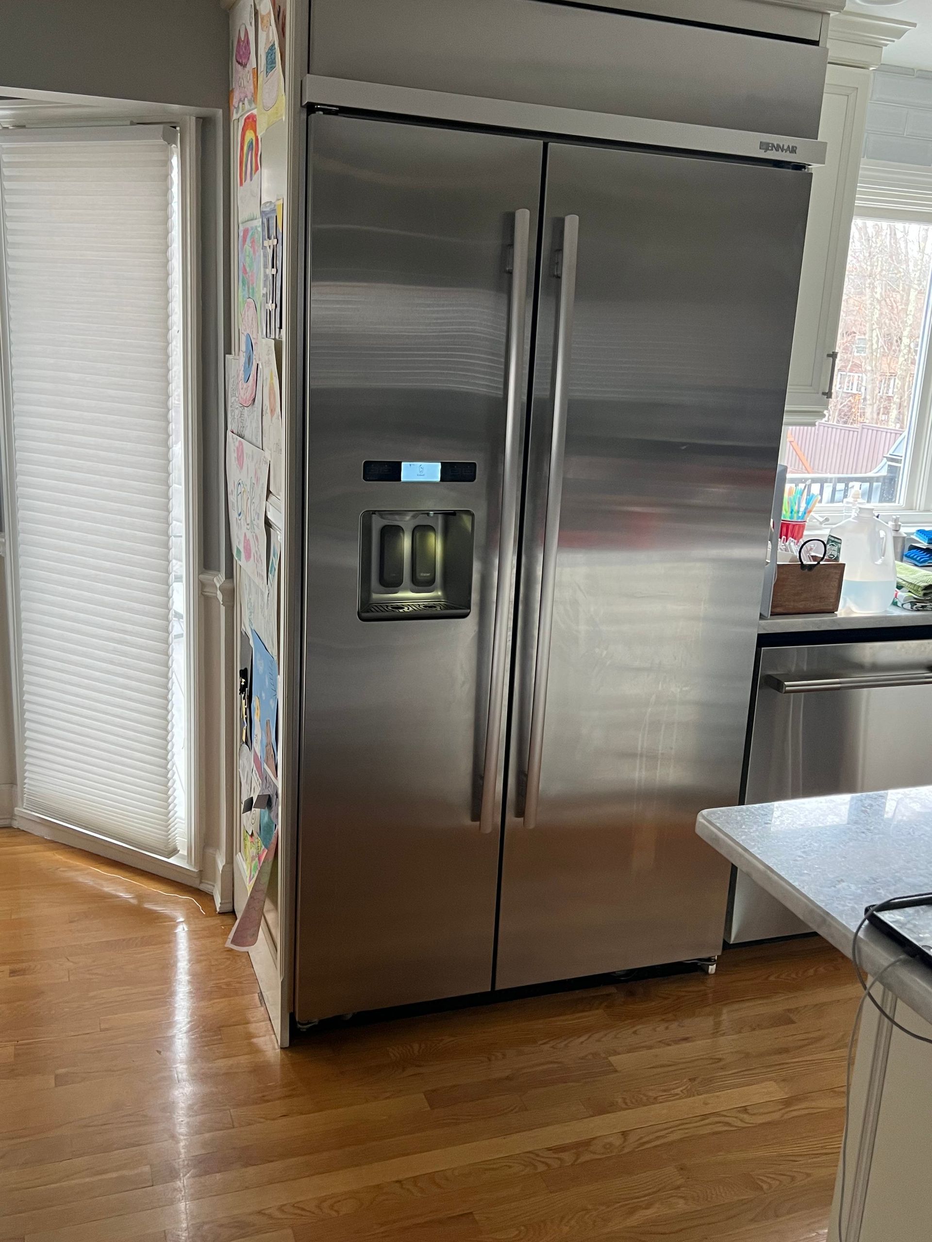 A stainless steel refrigerator is sitting in a kitchen next to a window.