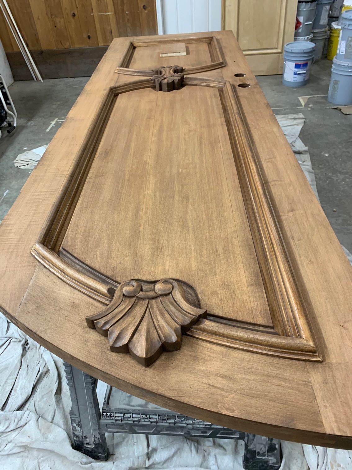 Wooden decorative cabinet door panel with carved border and shell motif on a workbench in a workshop.