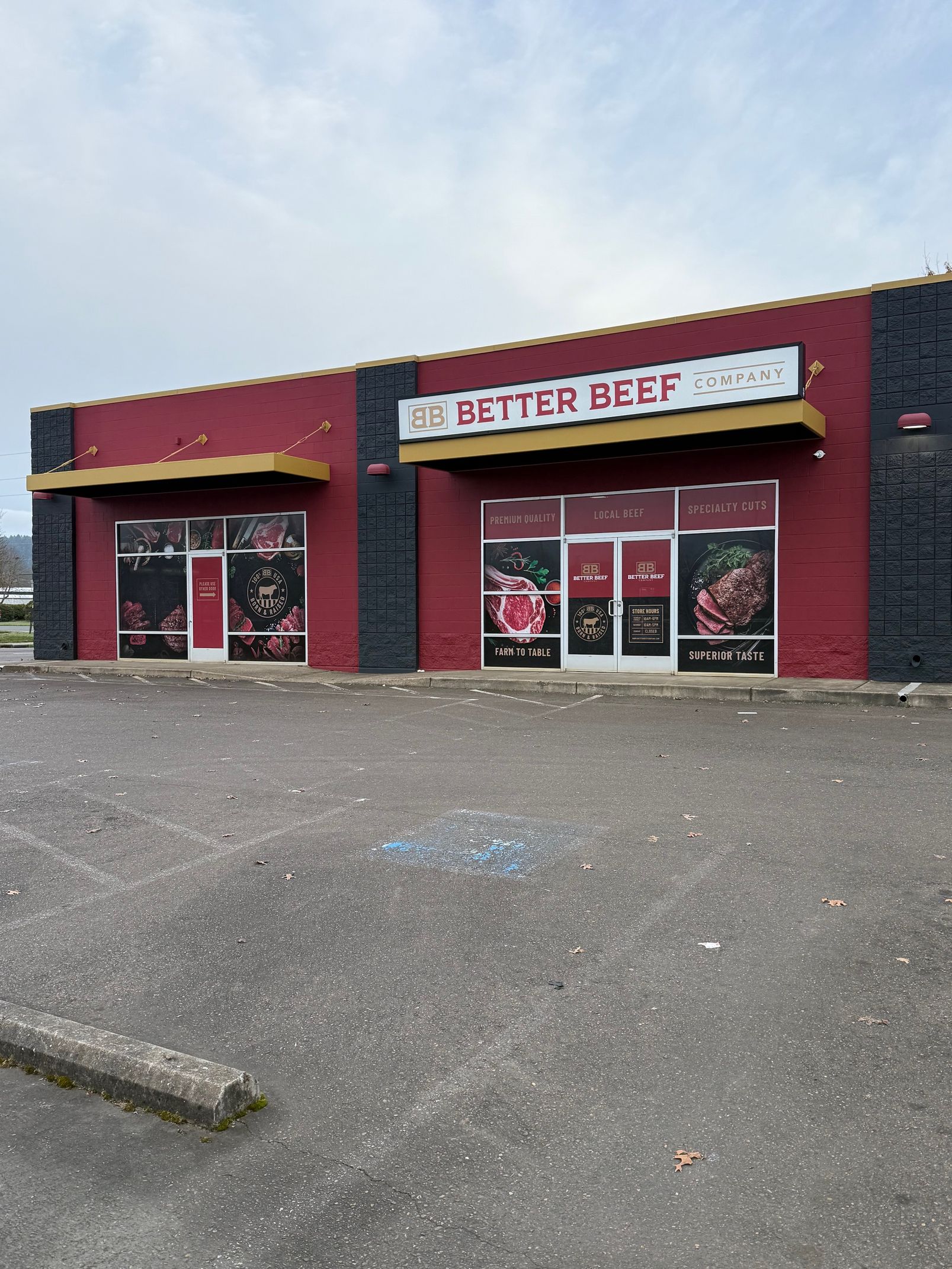 Red storefront with a sign reading “Be Better Be…”, pink-framed windows, and a gravel parking lot.