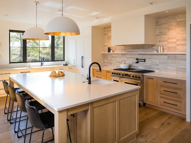 Modern kitchen with wood cabinets, white island, black stools, and large window lighting