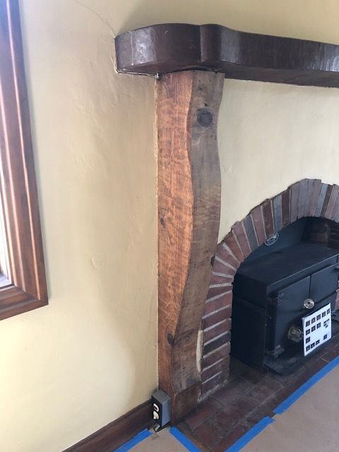 Wooden support post beside a brick fireplace mantel, with blue tape on the floor and wall.