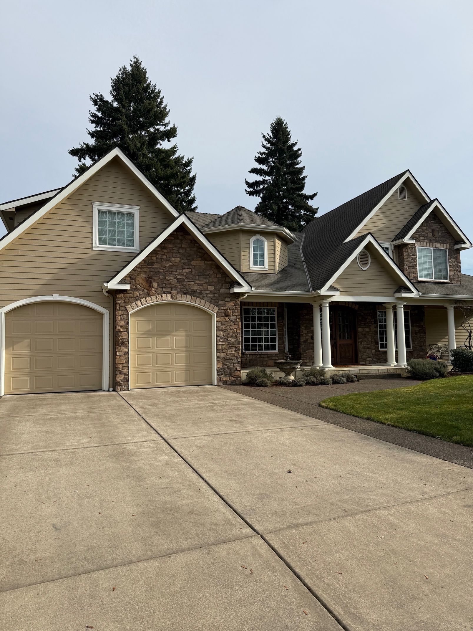 Suburban tan house with two garage doors, steep gables, and a wide concrete driveway