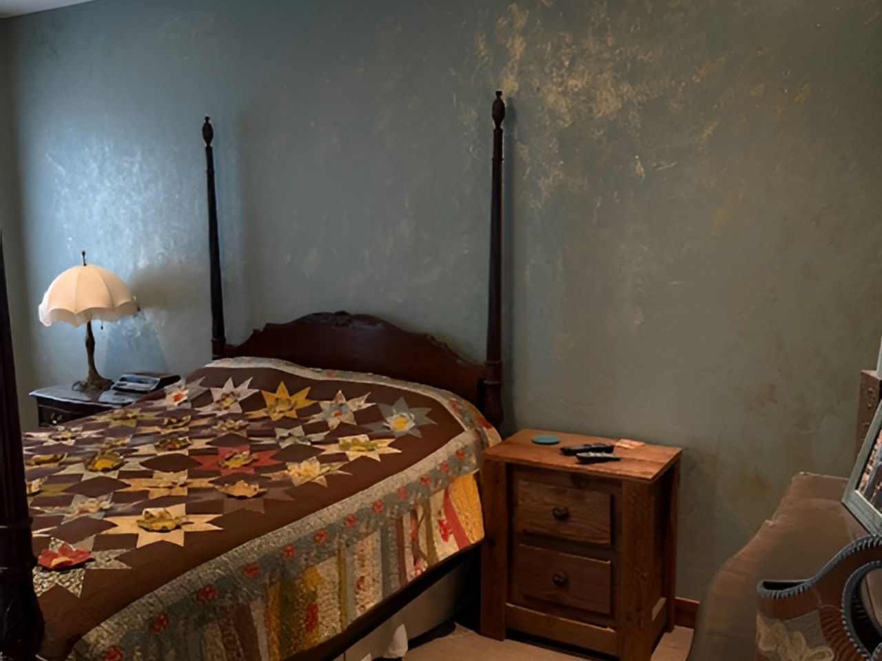 Bedroom with a four-poster bed, quilt, nightstand, lamp, and guitar against a gray wall