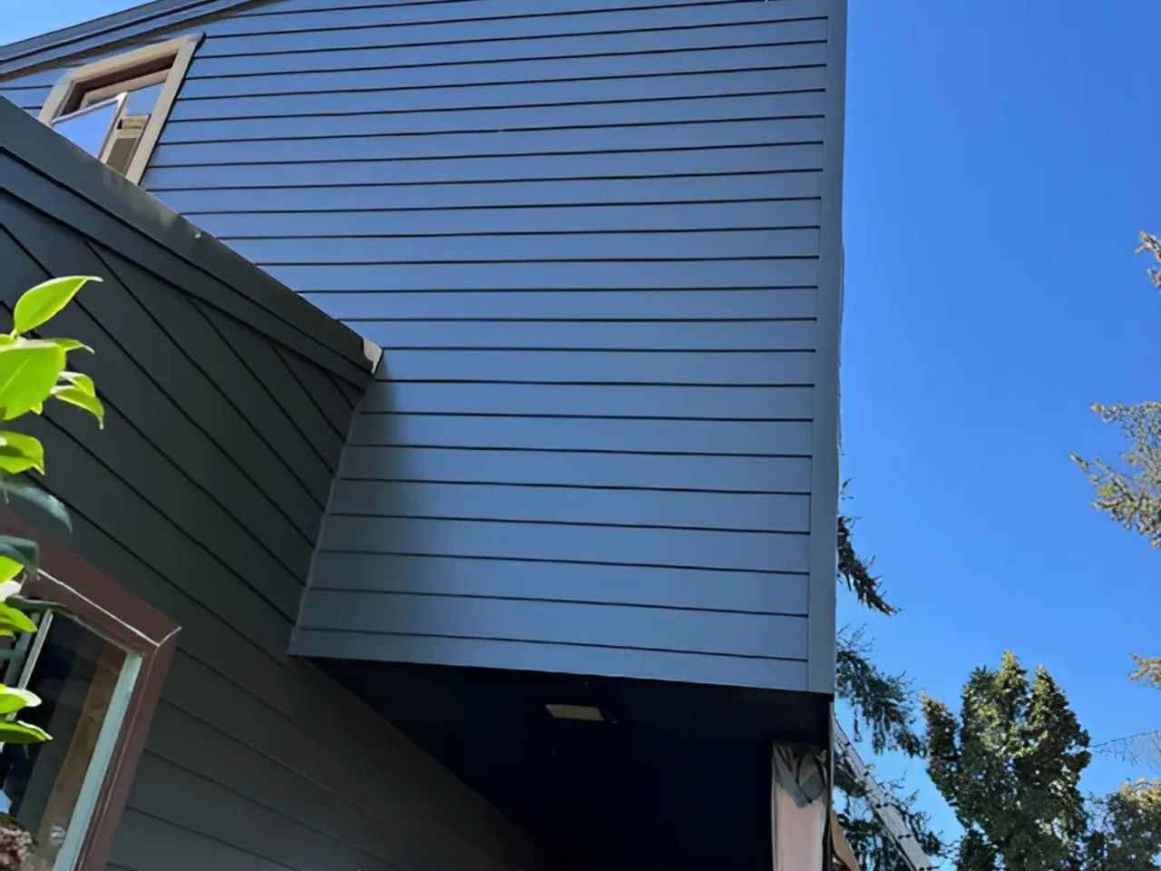 Blue house exterior with horizontal siding, roofline, and windows against a clear sky