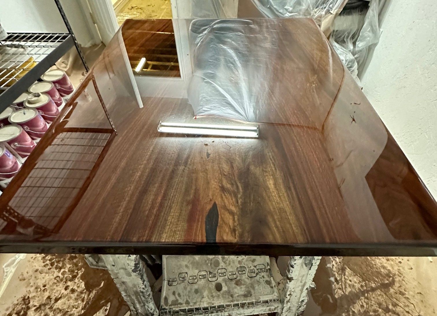 Glossy brown rectangular table with a plastic-wrapped item in the center, beside a tray of cupcakes in a bakery setting