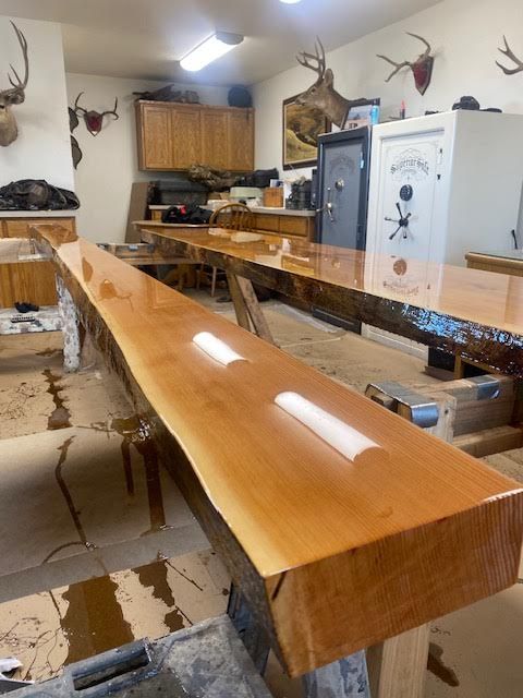 Glossy live-edge wooden bench in a rustic room with mounted deer heads and a white appliance in back