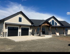 Modern single-story house with attached garage, light siding, dark roof, and a wide driveway under a blue sky