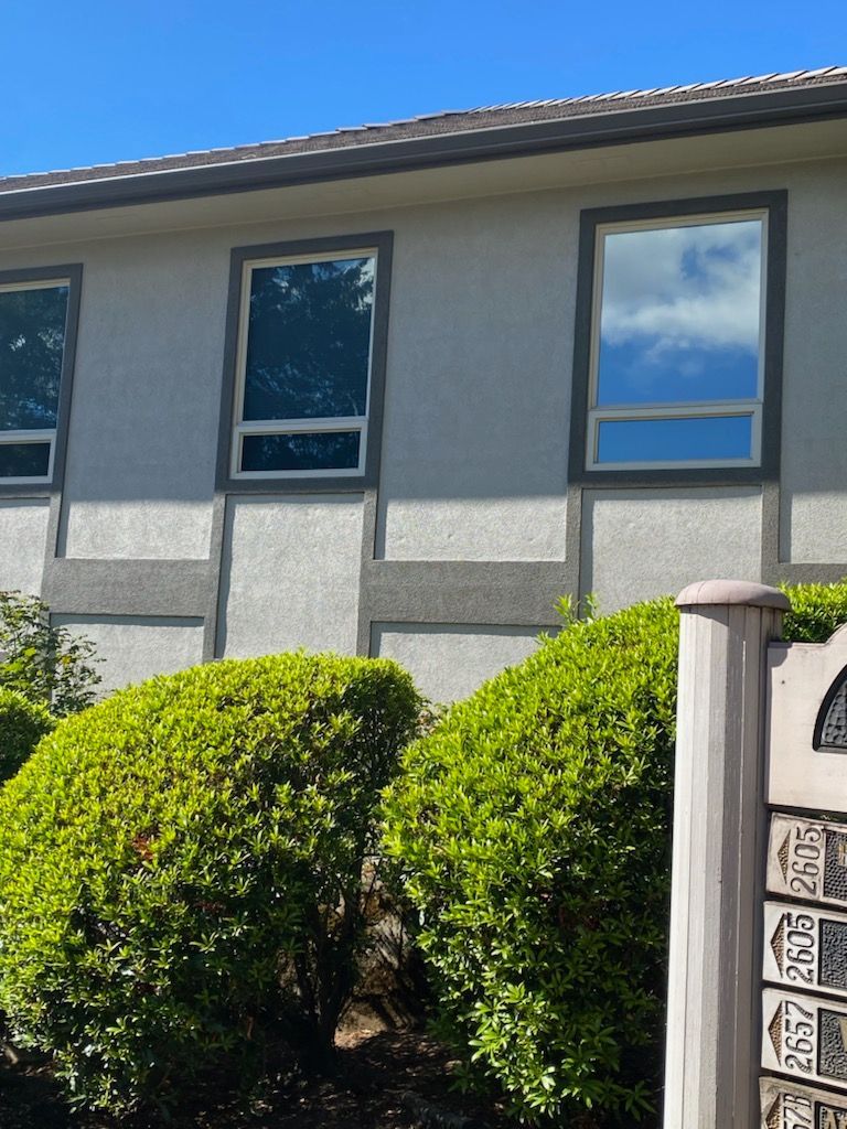 Exterior of a gray house with dark windows and neatly trimmed green shrubs in front