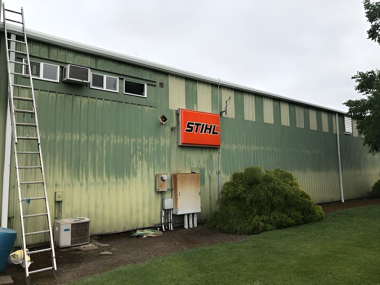 Exterior of a green industrial building with a red STIHL sign and a ladder on the left