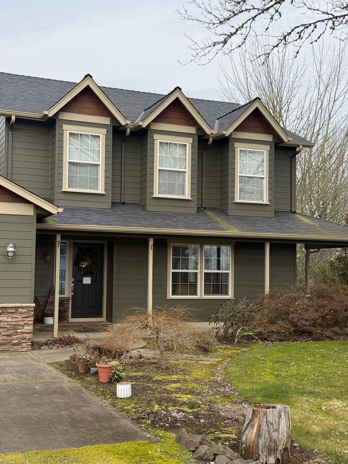 Two-story dark gray house with three gables, a covered porch, and a front yard in early spring.