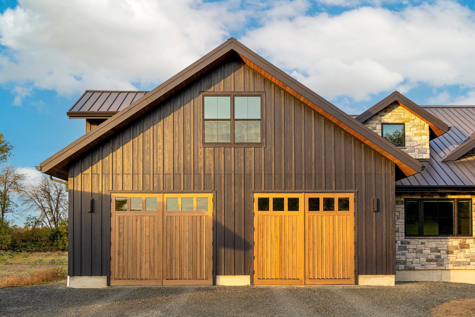 Wooden barn-style house with two garage doors and a gabled roof under a blue sky