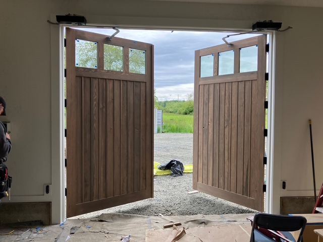 Open wooden barn doors framing a view of green fields and cloudy sky beyond