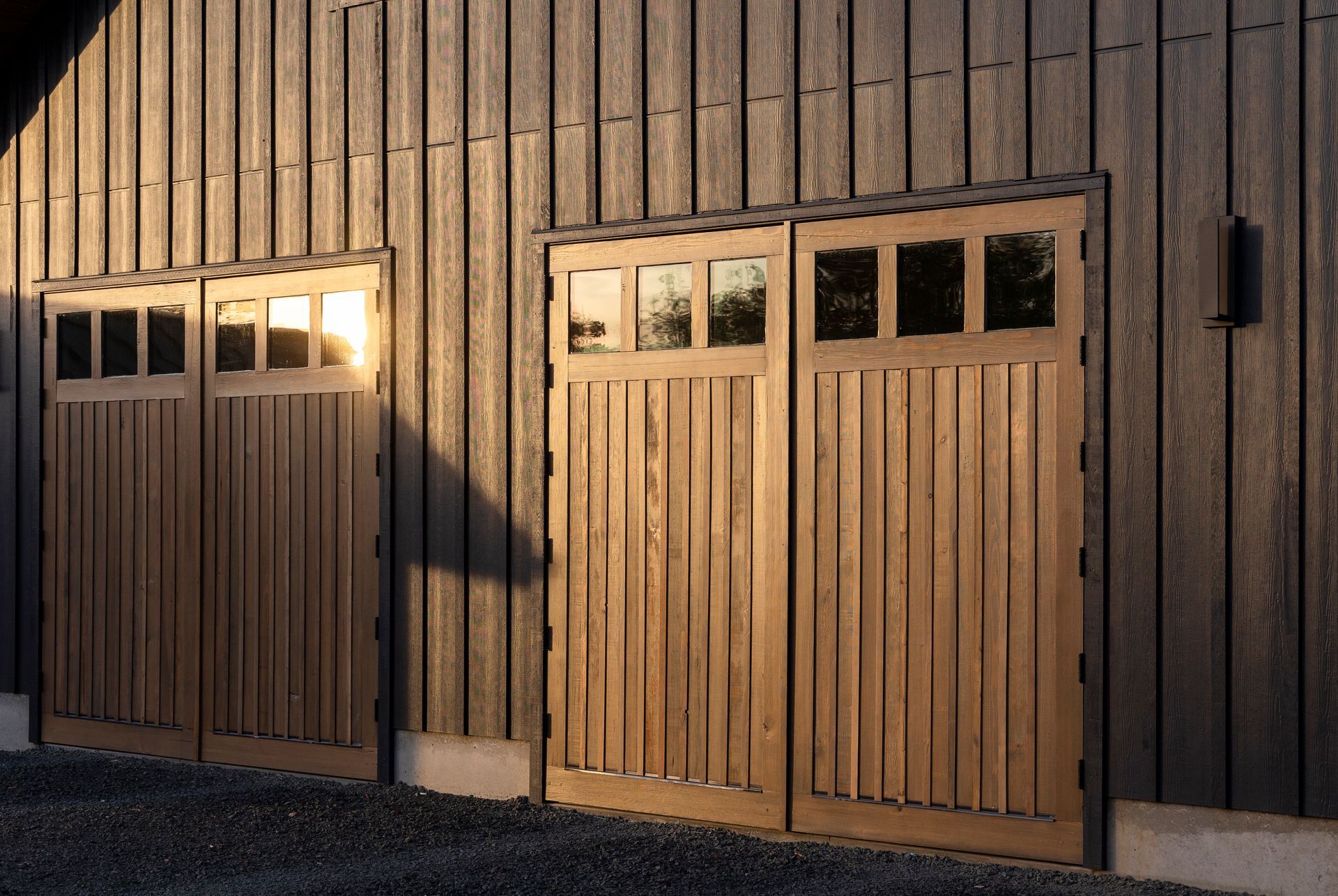 Wooden barn doors on a sunlit building exterior, with a small window and strong shadow.