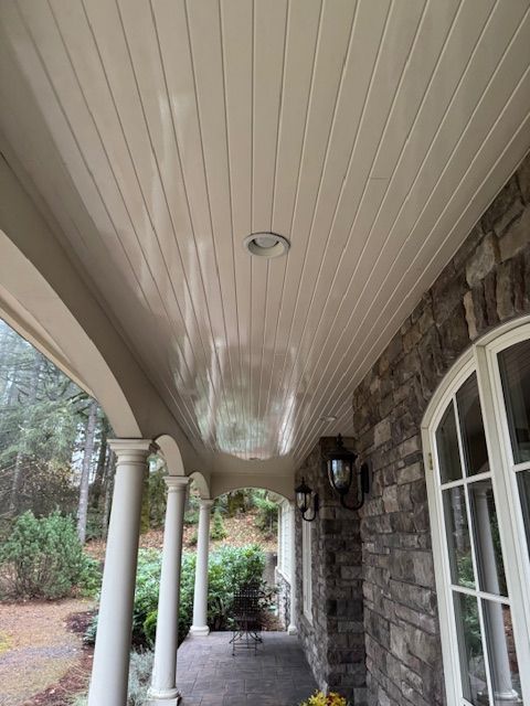 Covered stone front porch with white columns, arched ceiling, and wall lantern beside a windowed entry.