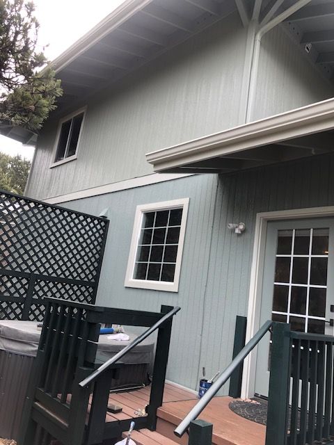 Two-story gray house exterior with white-trimmed windows, deck railing, and patio umbrella