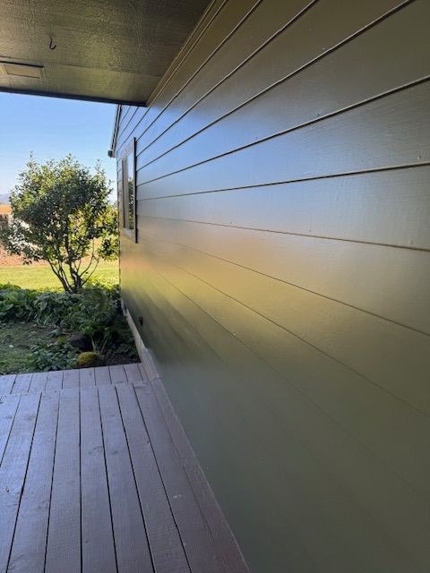 Covered porch beside a green lawn, with tan horizontal siding and a wooden deck in the foreground