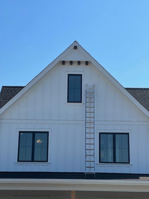 White house gable with dark windows and a ladder leaning up the front exterior wall