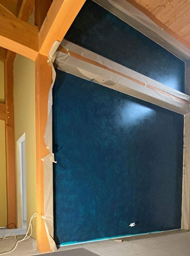 Blue window or wall panel in an attic with exposed wooden beams and insulation tape under a sloped ceiling