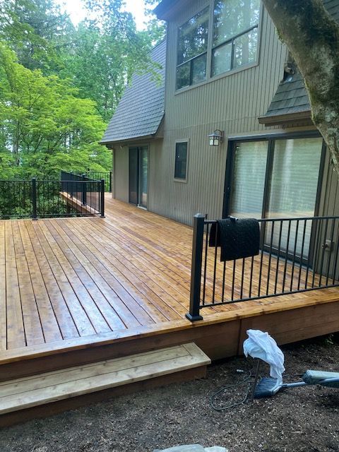 Wooden deck beside a house with black railing, steps, and forested yard beyond