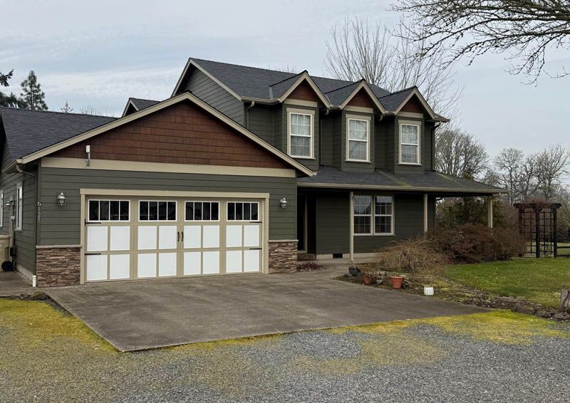 Suburban two-story house with gray siding, brown roof, and white double garage on a cloudy day
