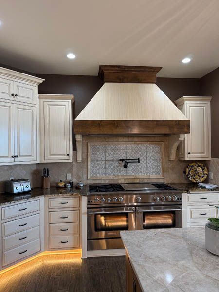 Modern kitchen with white cabinets, stainless range, wood hood, and soft under-cabinet lighting