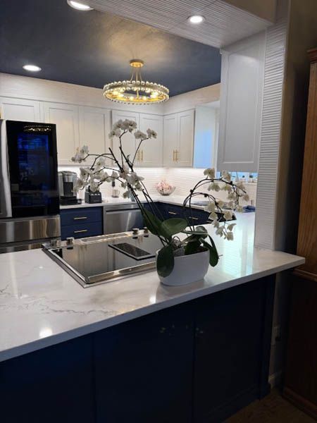 Modern kitchen with white cabinets, dark island, stainless appliances, and white orchids on the counter