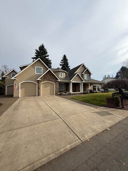 Suburban house with beige siding, two-car garage, and a wide concrete driveway under a cloudy sky