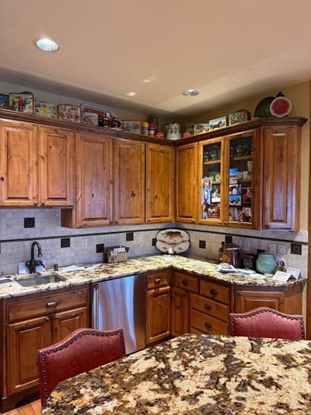 Wooden kitchen with granite countertops, tiled backsplash, and glass-front cabinets in warm lighting