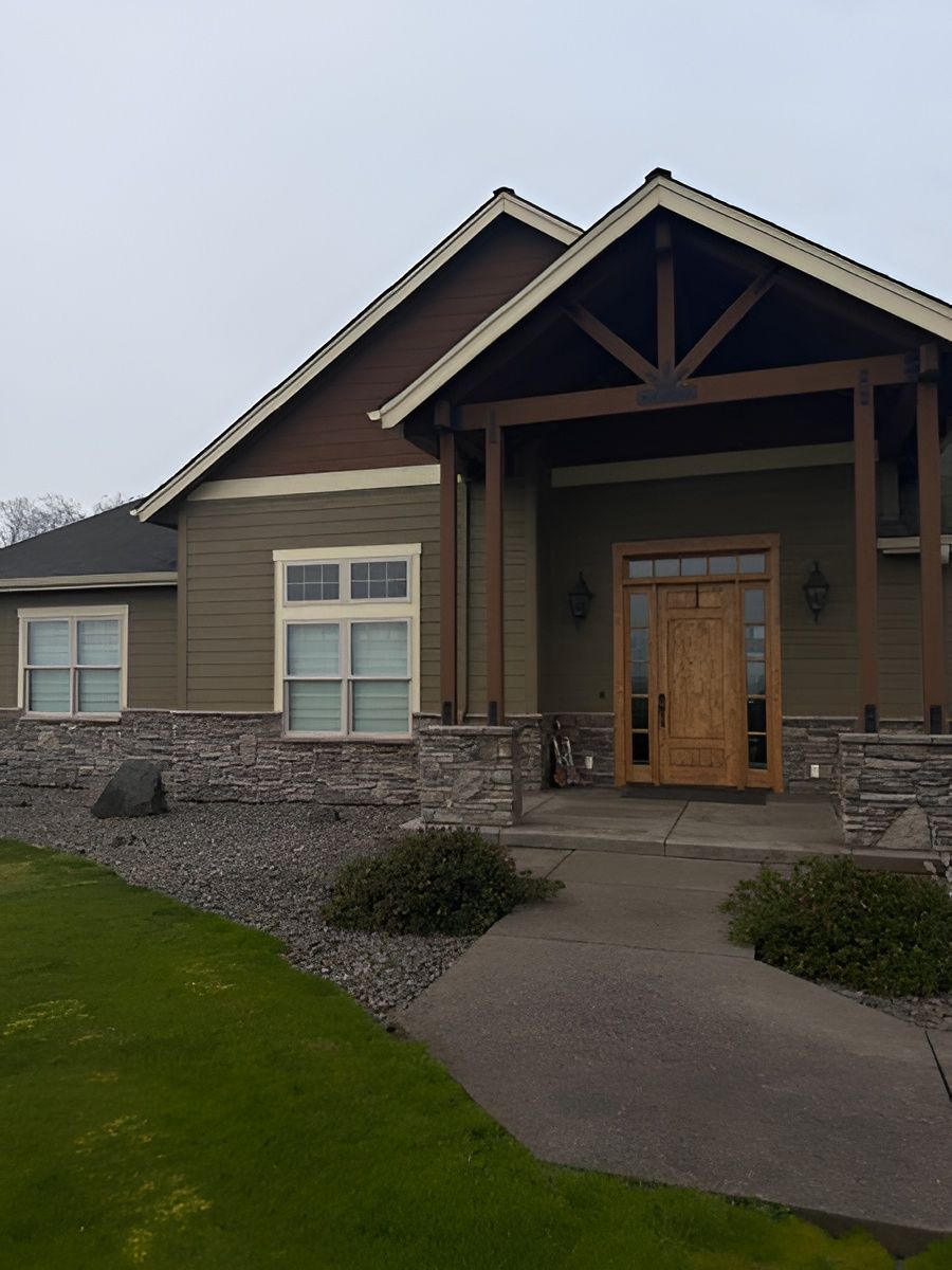 Single-story house with a covered front porch, stone landscaping, and a curved concrete walkway.