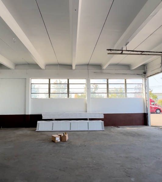 Empty warehouse interior with white beams, windows, stacked boards, and small boxes on the floor