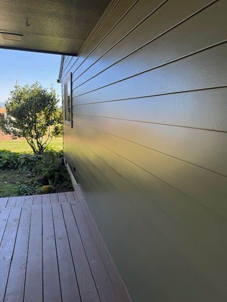 Covered porch beside green lawn and tree, with light wood siding and deck flooring.
