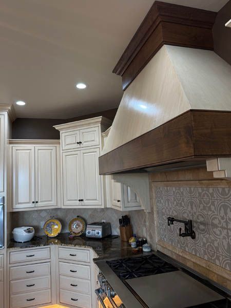 Bright kitchen with white cabinets, dark countertops, and a large stainless range hood above a stove.