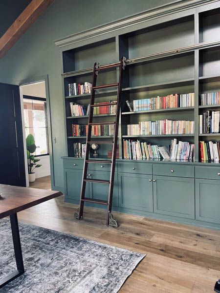 Built-in bookshelves with a ladder in a teal room beside a dining table and rug
