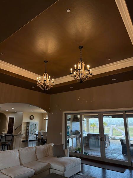 Spacious living room with brown ceiling, chandelier lights, and glass doors opening to a patio and pool