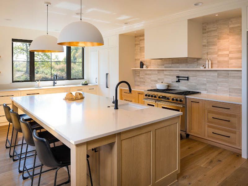 Modern kitchen with white island, wood cabinets, black bar stools, and large windows
