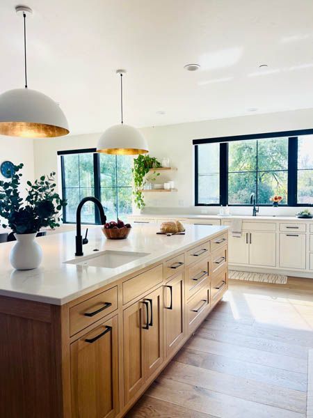 Bright modern kitchen with wooden island, white cabinets, and large windows overlooking greenery