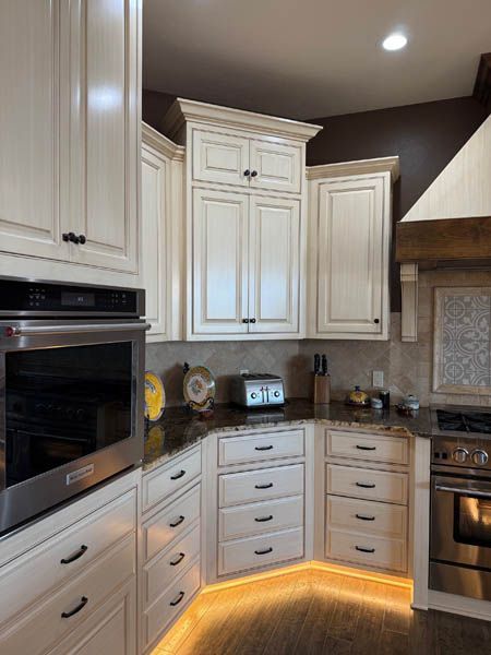 Compact kitchen corner with white cabinets, built-in oven, and warm under-cabinet lighting.