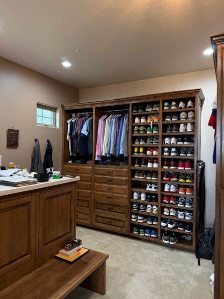 Walk-in closet with built-in shelves, hanging clothes, and rows of shoes beside a wooden bench.