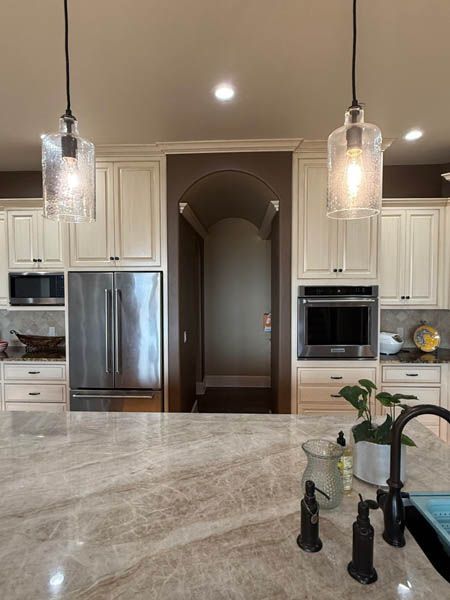 Modern kitchen with marble island, stainless steel appliances, cream cabinets, and pendant lights