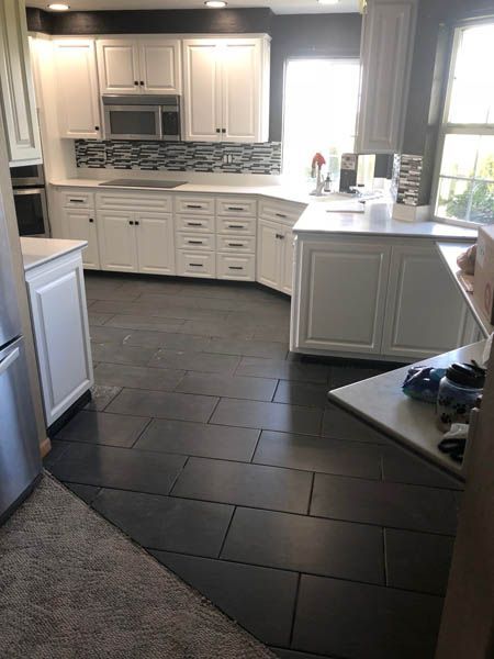 Bright white kitchen with dark tile floor, cabinets, and a window by the sink.