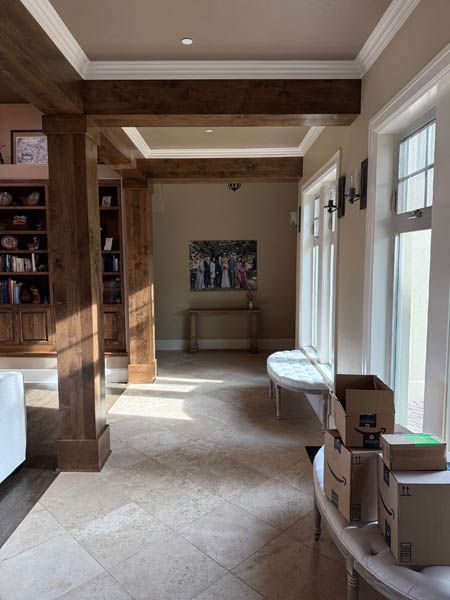 Bright hallway with wood beams, beige tile floor, window seats, and stacked boxes near the wall.