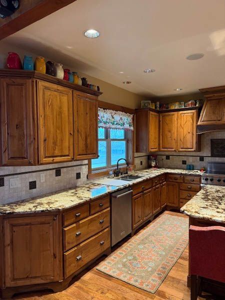Wooden kitchen with granite counters, center island, stainless dishwasher, and a window over the sink.