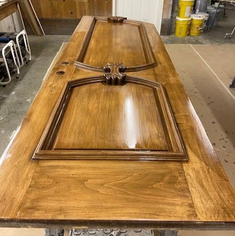 Wooden coffin lid with ornate cross, resting on a workbench in a workshop