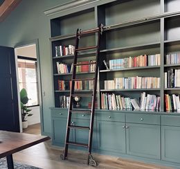 Blue-green built-in bookshelves with a dark wood ladder in a bright living room.