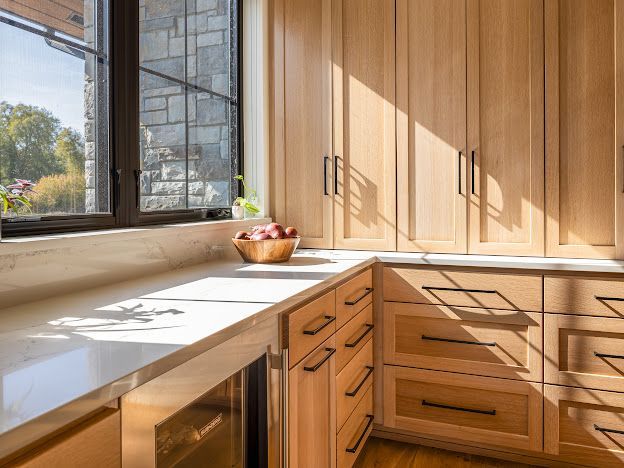 Sunlit modern kitchen with wood cabinets, white countertops, and a large window